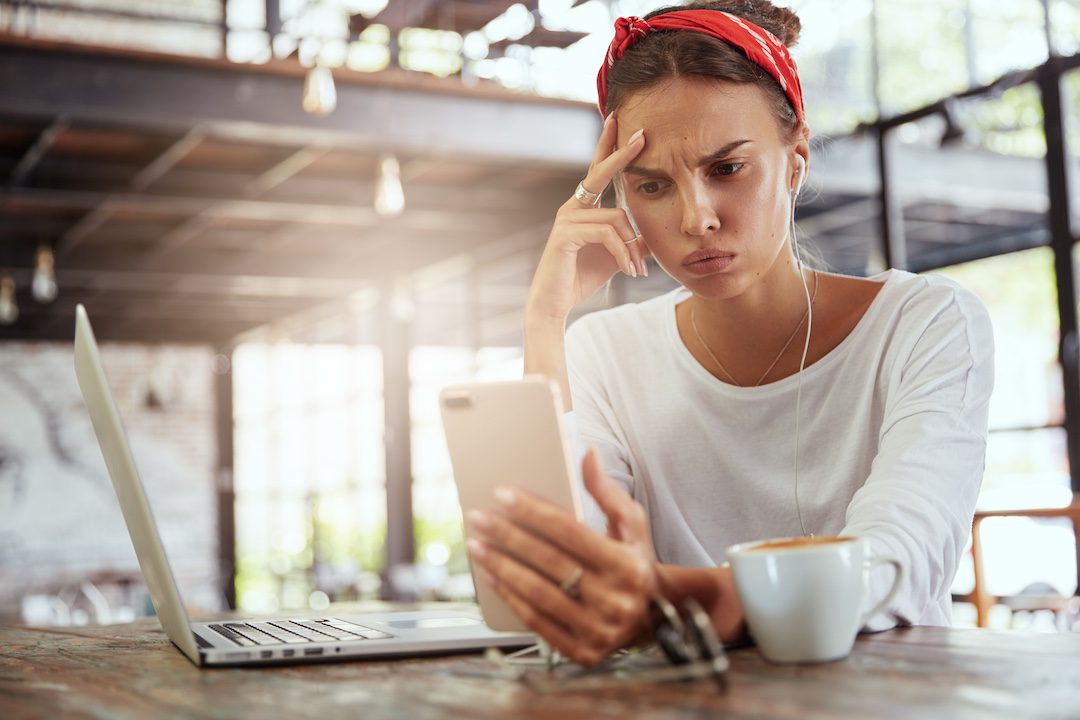 Jeune femme perplexe regardant son smartphone, confrontée à un problème de connexion au réseau Wi-Fi.