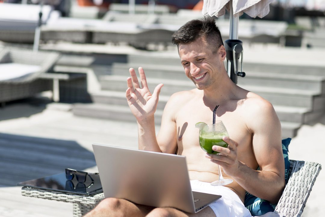 Homme souriant travaillant sur son ordinateur portable en extérieur grâce à une bonne connexion Wi-Fi.