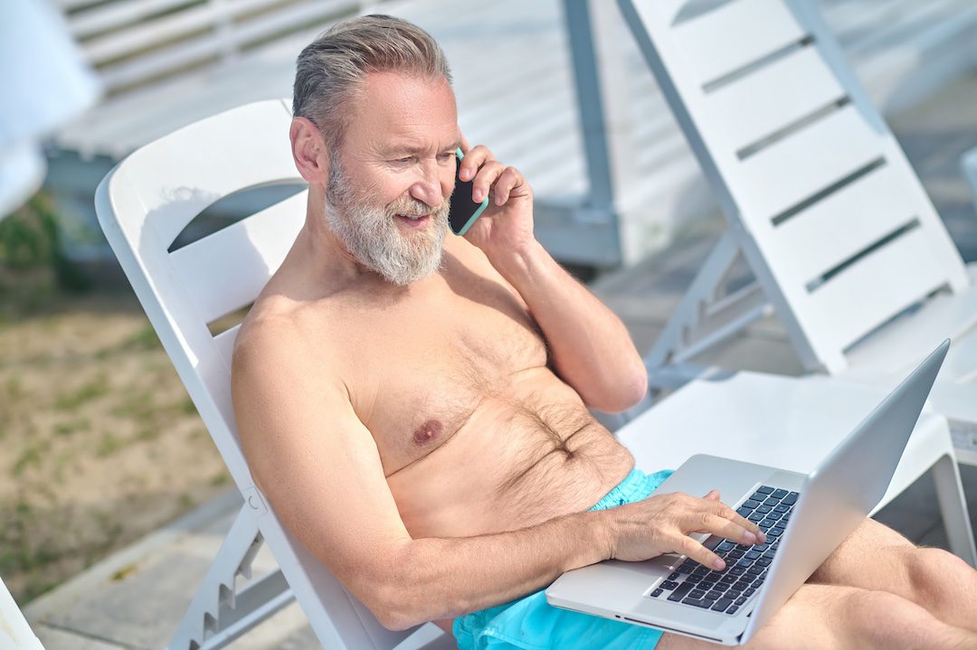 Homme senior détendu utilisant son ordinateur portable et son téléphone en extérieur avec un réseau Wi-Fi étendu.